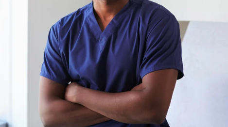 a close-up photo of a person wearing navy scrubs with their arms crossed; their face is not in frame.