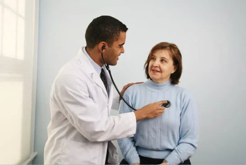 a person in a lab coat listening to a patient's heart with a stethoscope